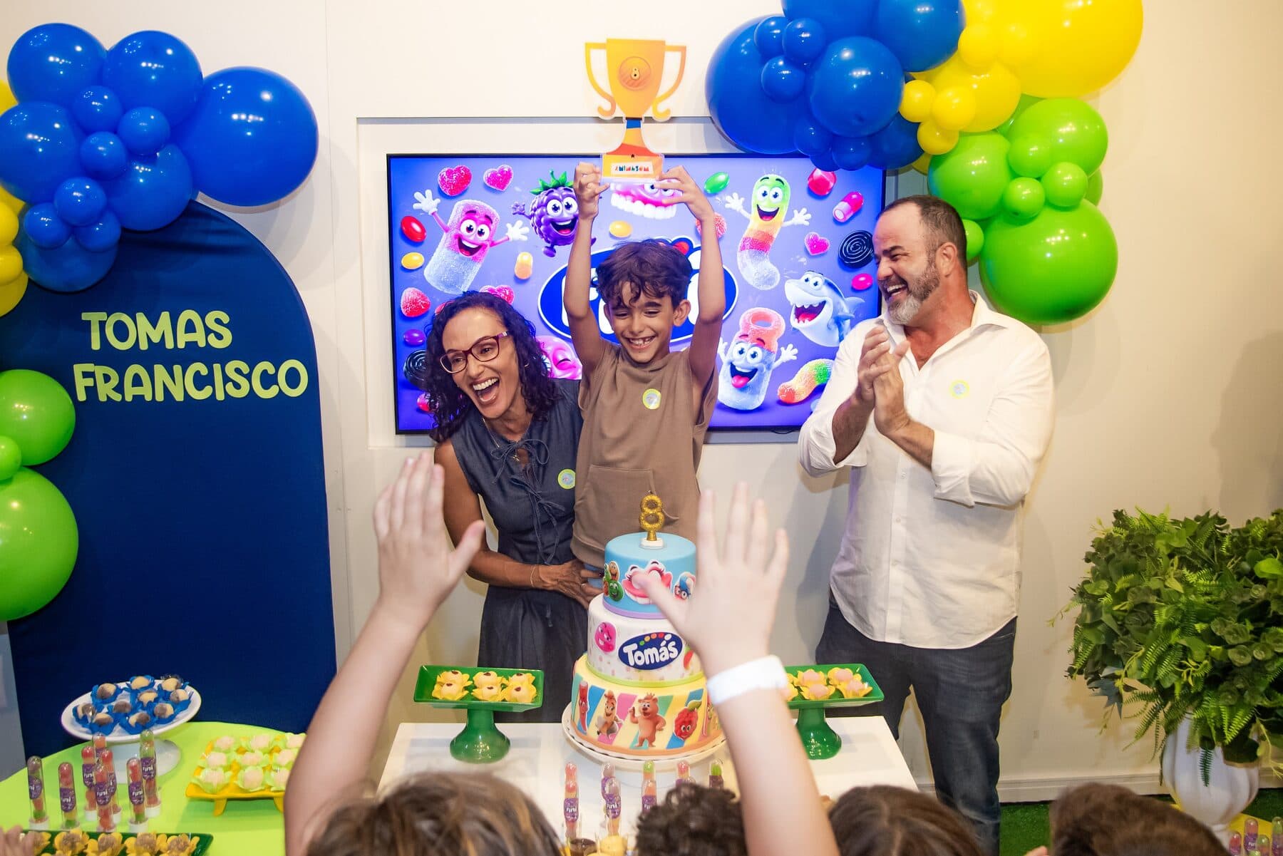 Aniversariante erguendo um troféu ao lado dos pais durante a festa