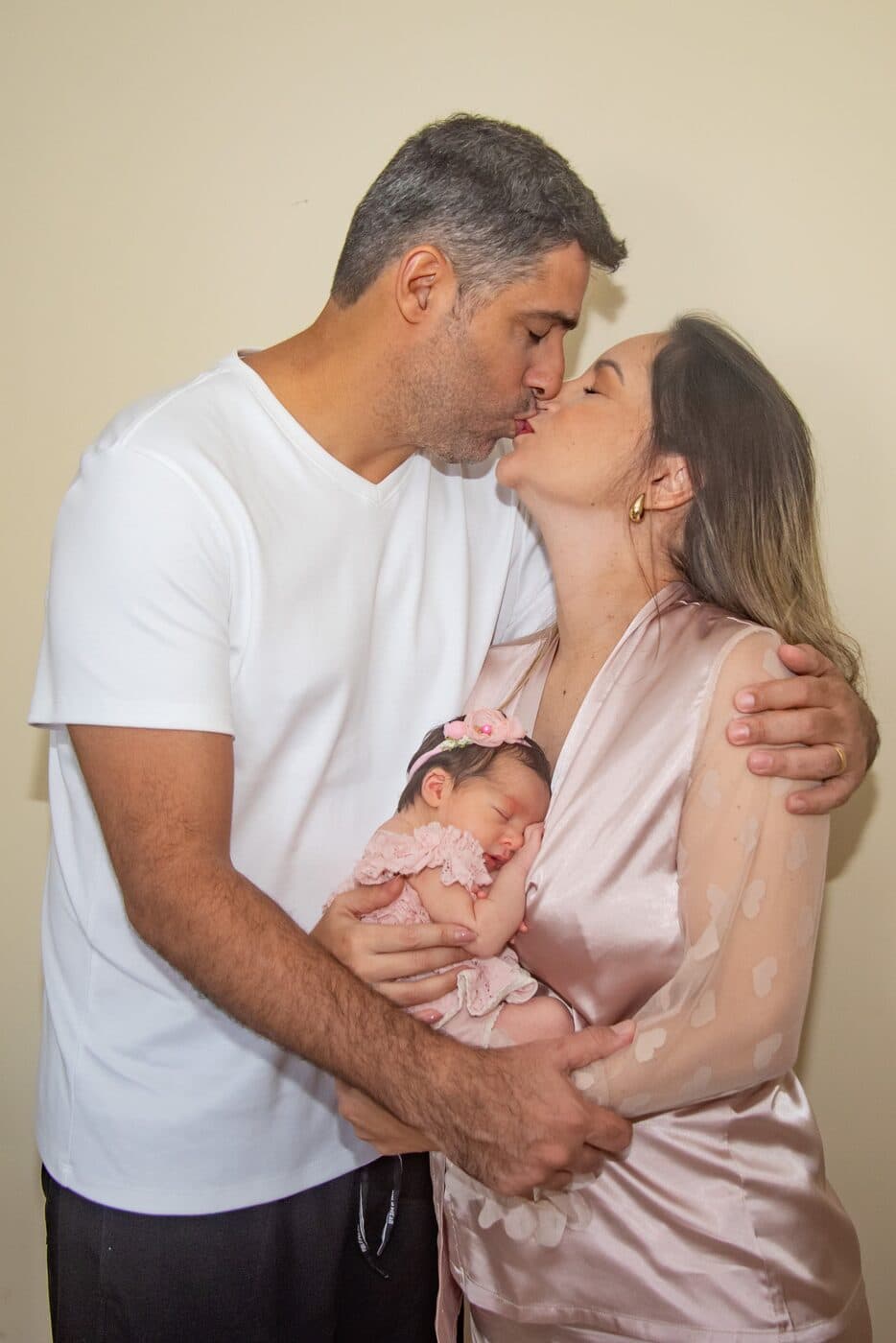 Casal se beijando com a filha recém-nascida no colo