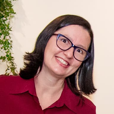 Retrato de Priscila Figueira sorrindo, de óculos e blusa vinho
